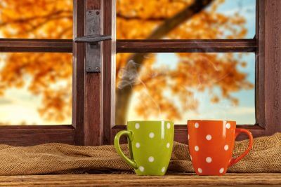 two coffee mugs in front of a window with a fall colored tree in the background